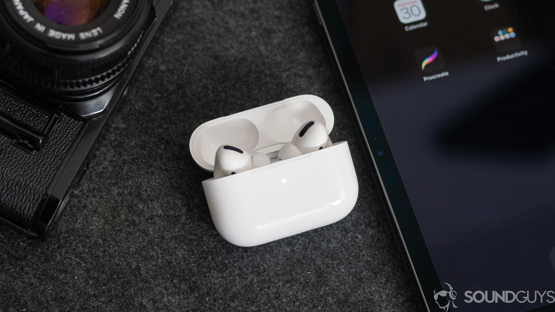 Apple AirPods Pro-1 The AirPods Pro earbuds in the wireless charging case next to an iPhone and digital camera.