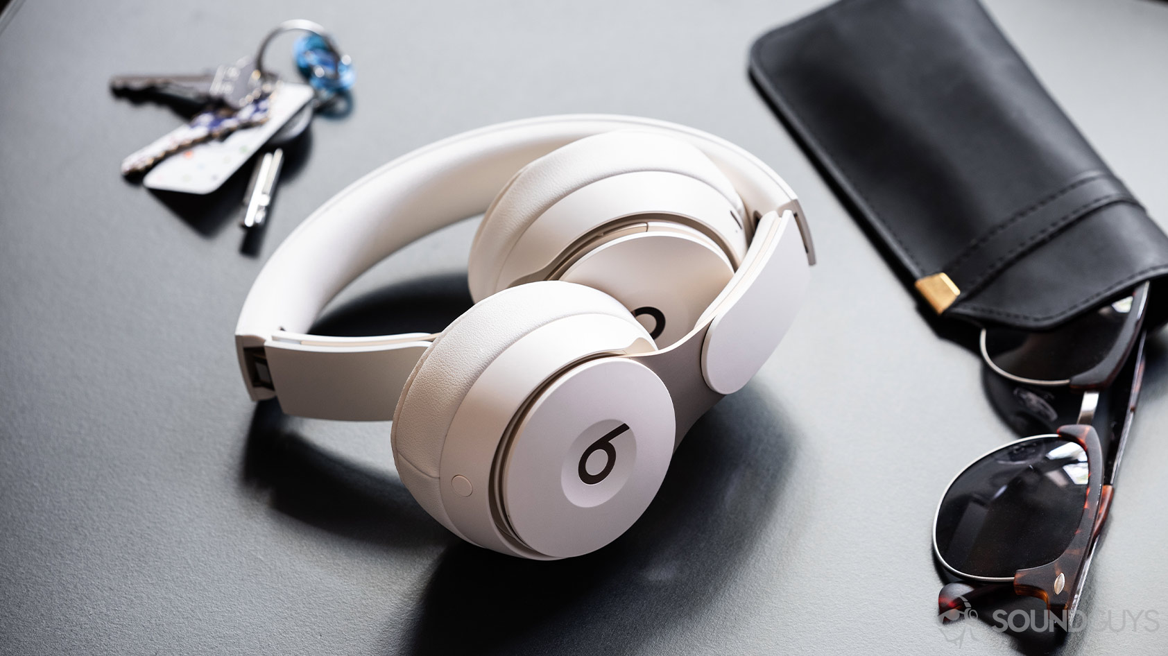 Beats Solo Pro-noise canceling headphones folded A photo of the Beats Solo Pro on-ear noise canceling headphones folded inward on a black surface and surrounded by sunglasses and keys.