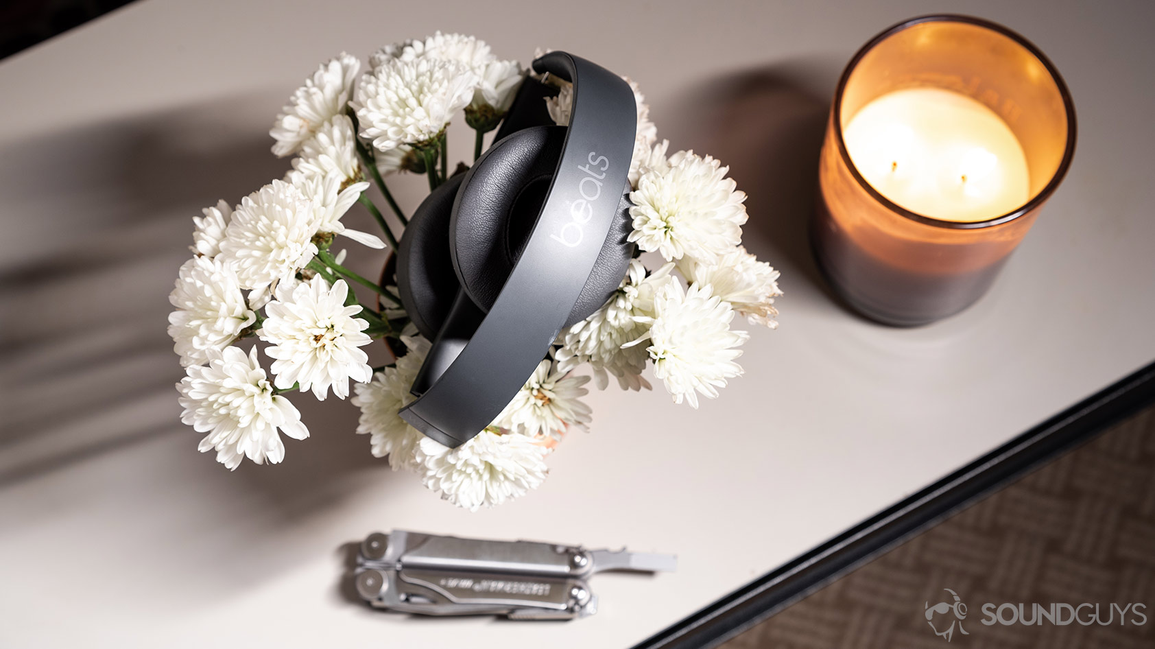 Beats Solo3 Wireless-on ear headphones grey folded A picture of the Beats Solo3 Wirless headphones folded atop a bed of flowers with a candle and multitool.
