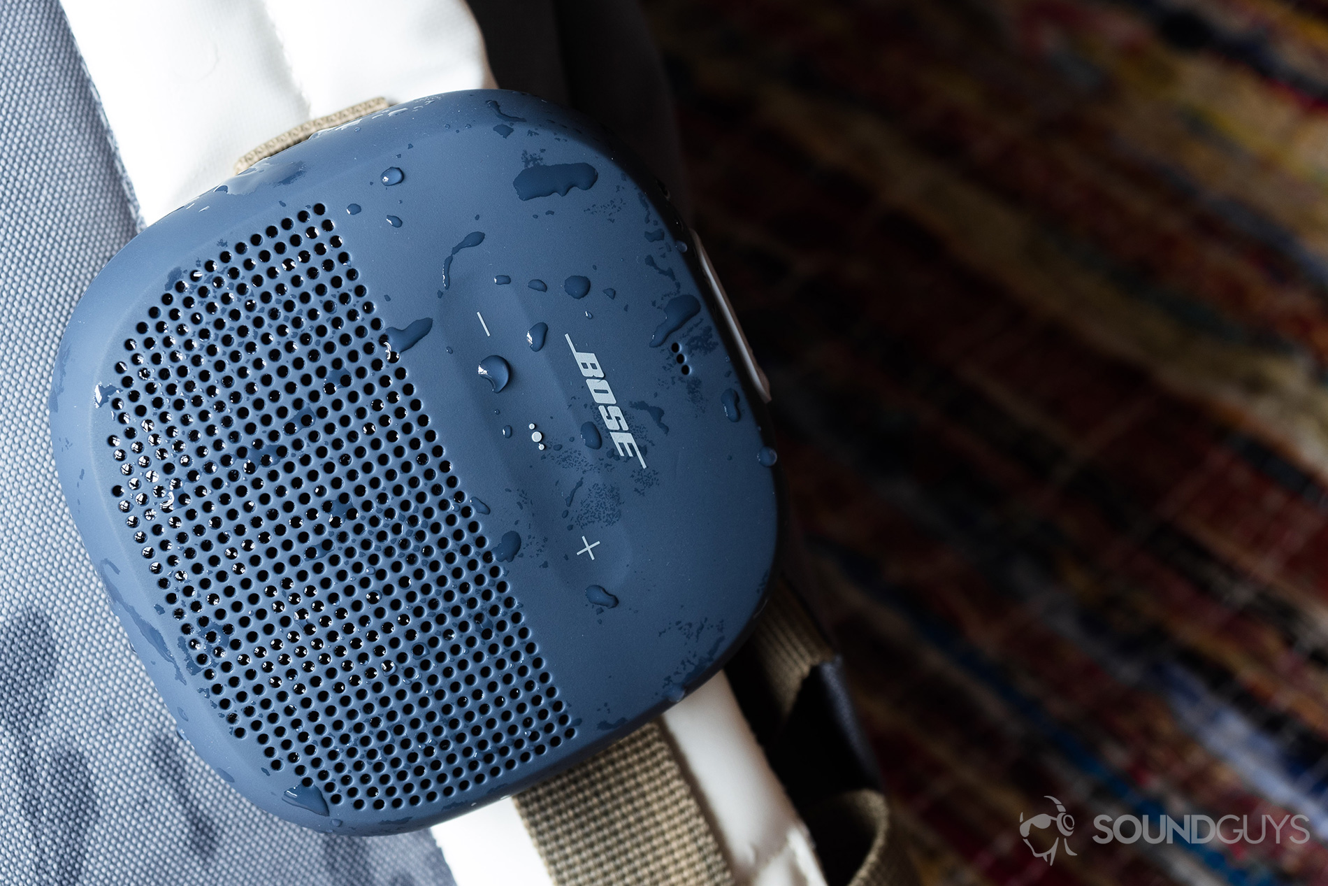 Bose_SoundLink Micro_ (1) Bose SoundLink Micro (blue) waterproof speakers hooked onto a white backpack.