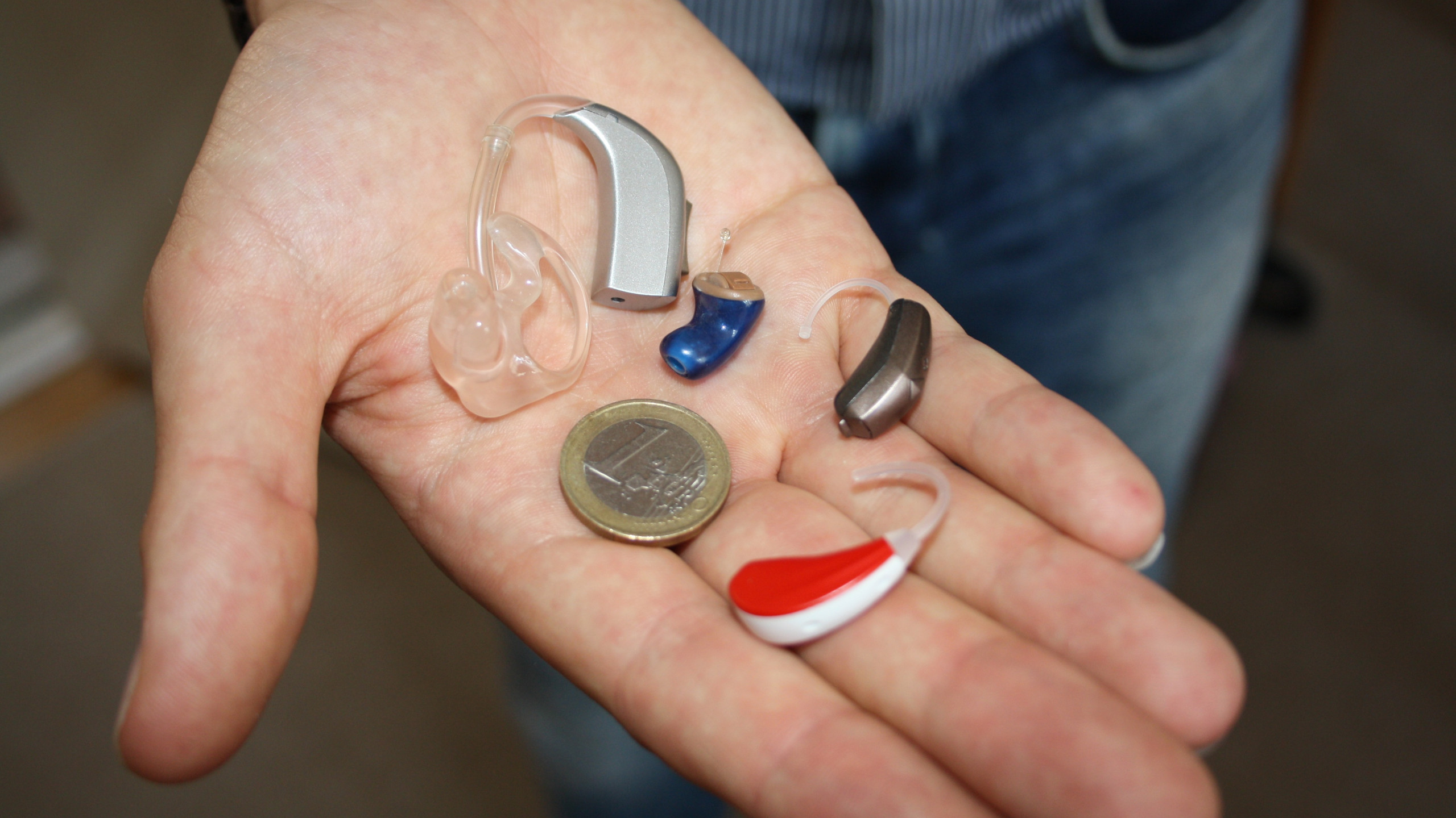 BTE and ITE Hearing Aids Man holding a selection of hearing aids and a one Euro coin.