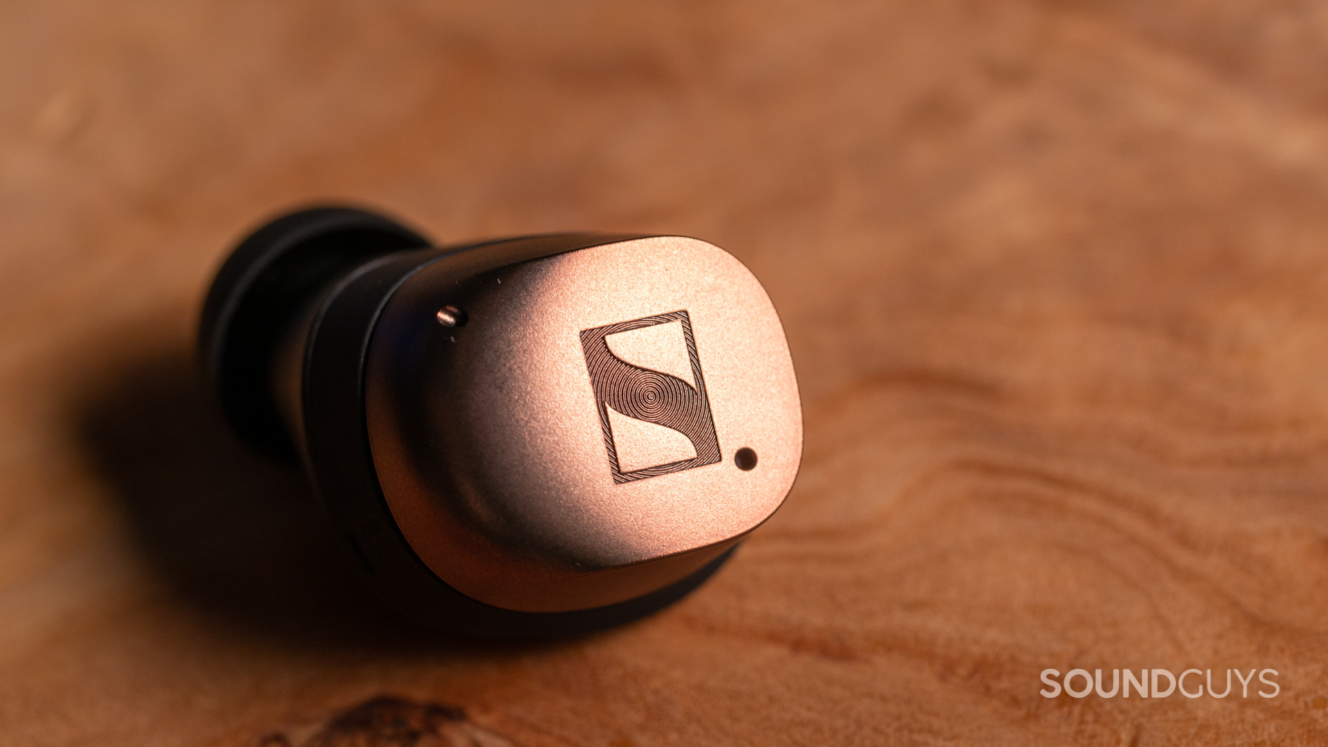 sennheiser-momentum-true-wireless-4-bud-vanity A close-up photo of the Sennheiesr MOMENTUM True Wireless 4's earbud on a wooden table.